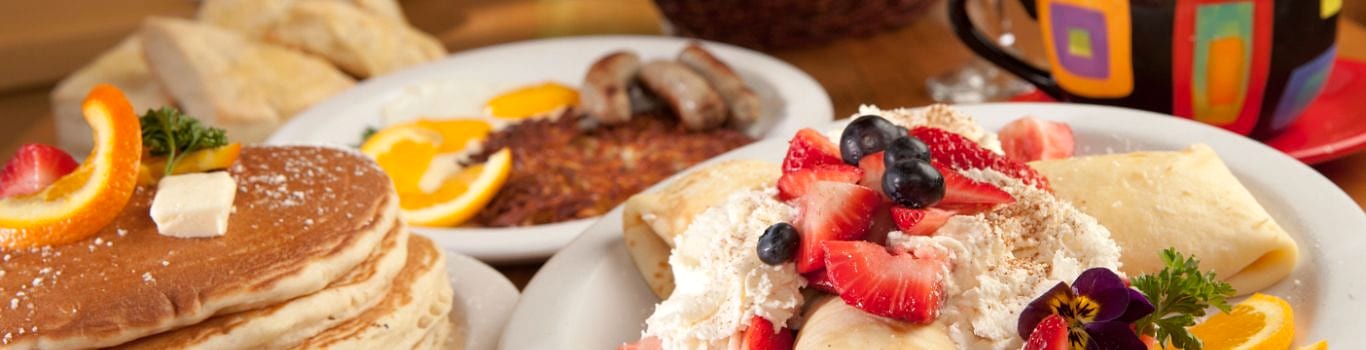 A breakfast spread of pancakes, crepes topped with berries and cream, eggs, sausages and hash browns